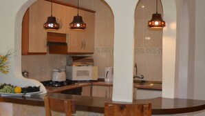 Una cocina con armarios de madera, microondas, cafetera y dos lámparas colgantes.