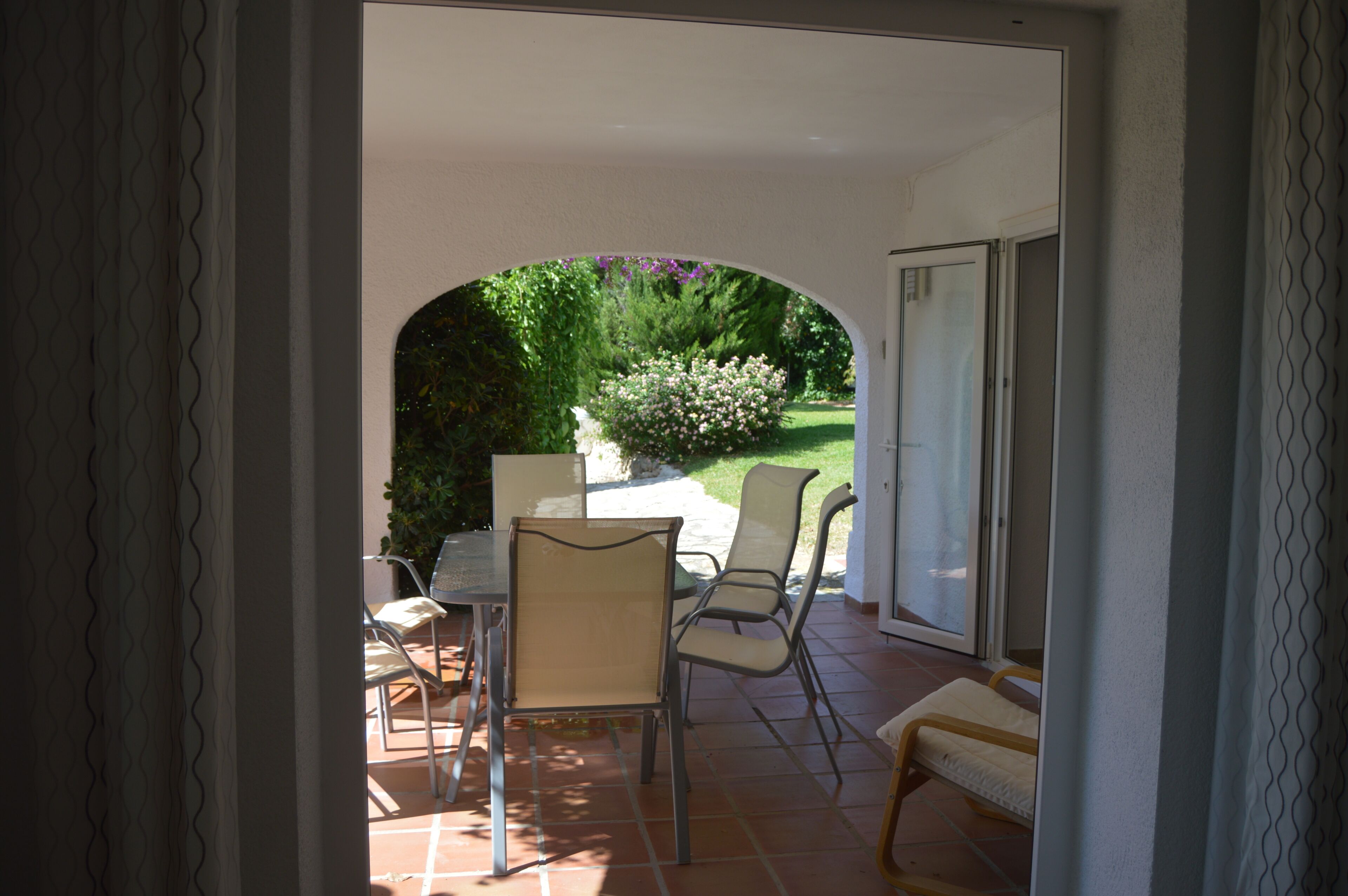 An outdoor patio with a table and chairs, a bench, and a view of a garden and trees.