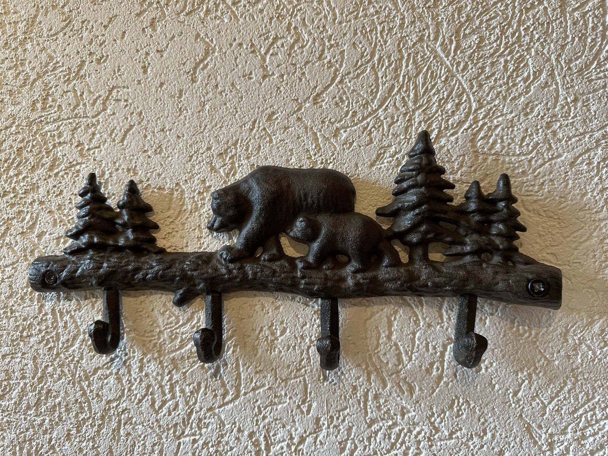Een metalen decoratie voor aan de muur, met een beer en bomen.