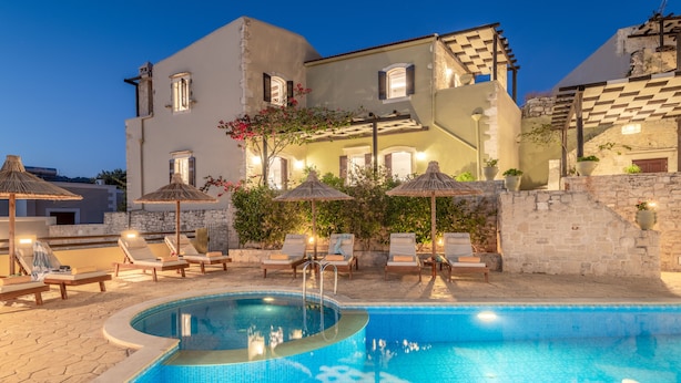 A swimming pool with lounge chairs and umbrellas, surrounded by stone walls and a building with multiple windows. - Dafni Villa, a Blissful Retreat with 40m² Pool (Rethymno)