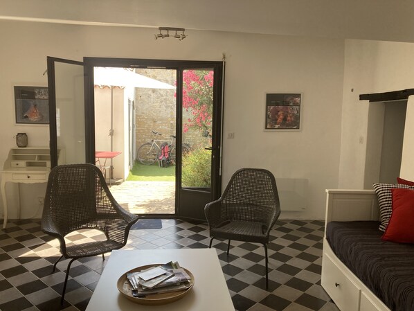 A room with two black mesh chairs, a white table with a tray of papers, a bed with a red pillow, and a checkered floor.
