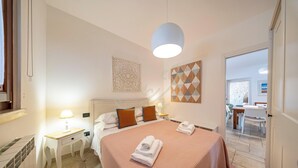 Ett hotellrum med en säng, sängbord, en lampa, en dekorativ väggdekoration och ett geometriskt väggkonstverk.