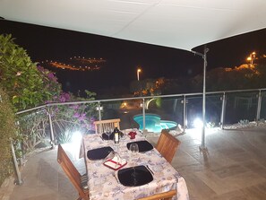 En uteservering med ett bord för fyra personer, med utsikt över en swimmingpool och en vacker vy över staden i kvällsljus.