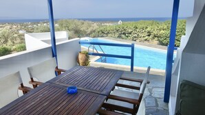 Una terraza con mesa y sillas de madera, una piscina y vistas al mar y edificios a lo lejos.