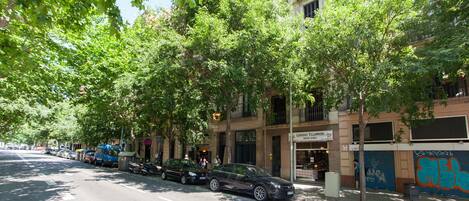 A street lined with trees and parked cars, with a building featuring a restaurant named 'Legumes Villarroel' on the ground floor.