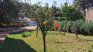 Un jardin avec un petit arbre, une balançoire et une structure de jeux verte.