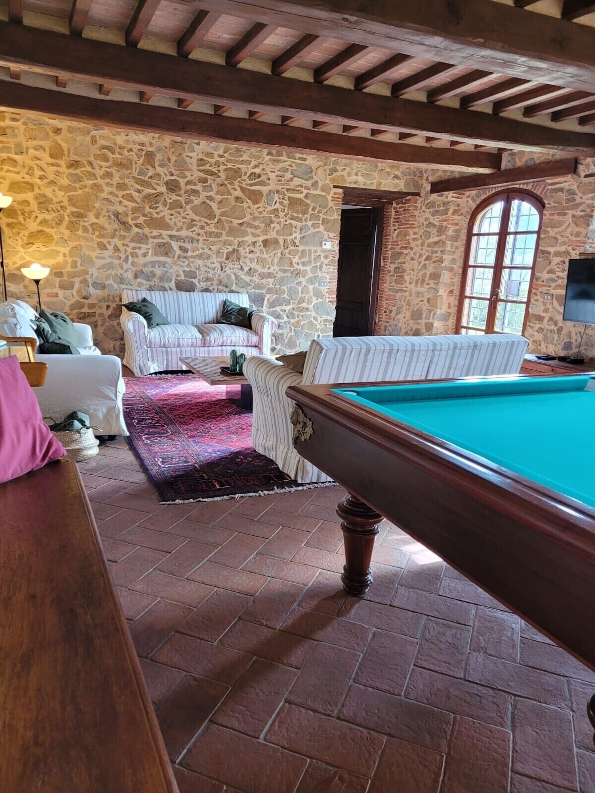 A cozy room with a pool table, stone walls, and a rustic wooden ceiling.
