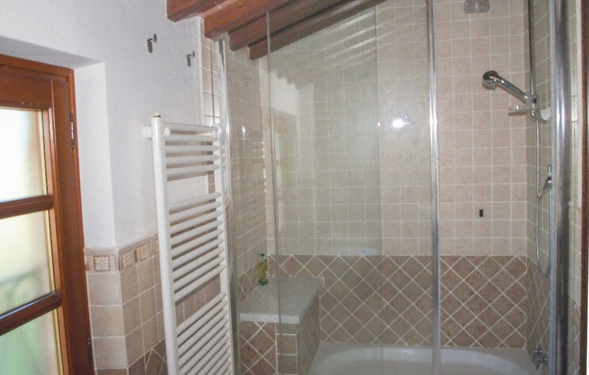 A bathroom with a glass-enclosed shower, a white bathtub, and a towel rack.