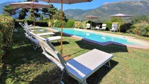 Un espace aménagé au bord de la piscine, avec des chaises longues et des parasols, entouré d’une pelouse bien entretenue et avec des montagnes en toile de fond.