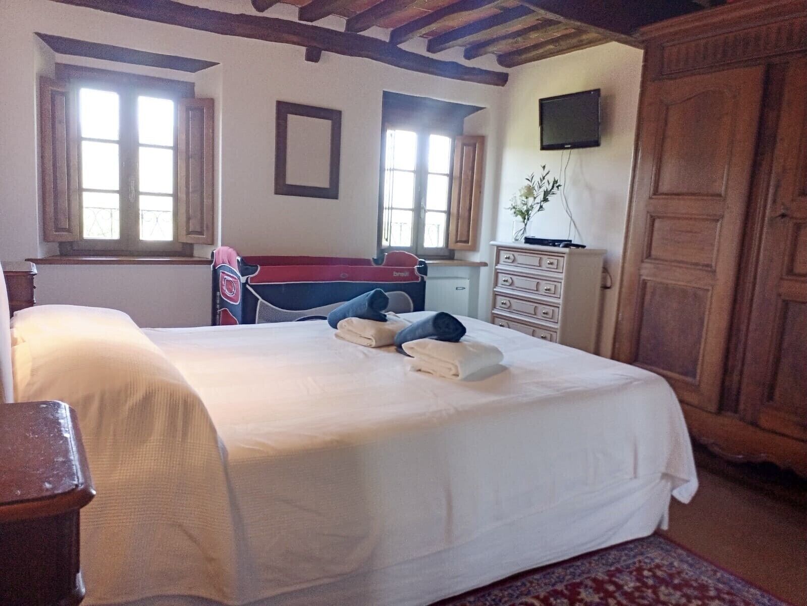 Een slaapkamer met een groot bed, een bureau, een dressoir en een televisie aan de muur.