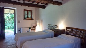 Une chambre avec deux lits, un plafond en bois, une fenêtre avec des rideaux, une lampe et une petite table sur laquelle est posée une plante.