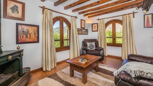 Un salon chaleureux avec des poutres en bois, une cheminée et de grandes fenêtres ornées de rideaux.