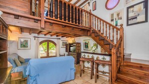 Un vaste espace de vie comprenant un escalier en bois, un canapé, une table à manger et un lit recouvert d’une couverture bleue.