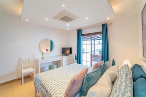 Un dormitorio con cama, escritorio, silla, televisor y ventana con cortinas.