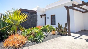 A modern house with a white exterior, a stone wall, and a wooden pergola.