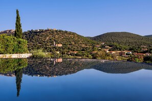Uma vista serena do lago, com reflexo límpido, uma cipreste imponente e um morro com edifícios dispersos.