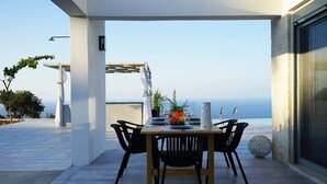 Espaço de refeições com mesa posta para quatro pessoas, com vista panorâmica do oceano.