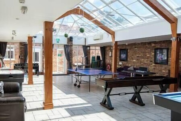 Un espace de loisirs intérieur comprenant une table de ping-pong, une table de billard et une table de jeu de fléchettes.