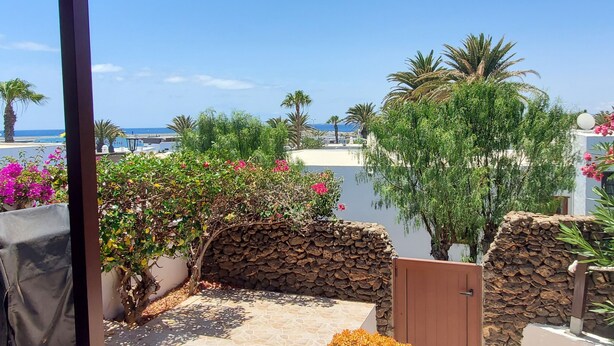 Un patio con suelo de piedra, pared de piedra y vistas al mar y palmeras.