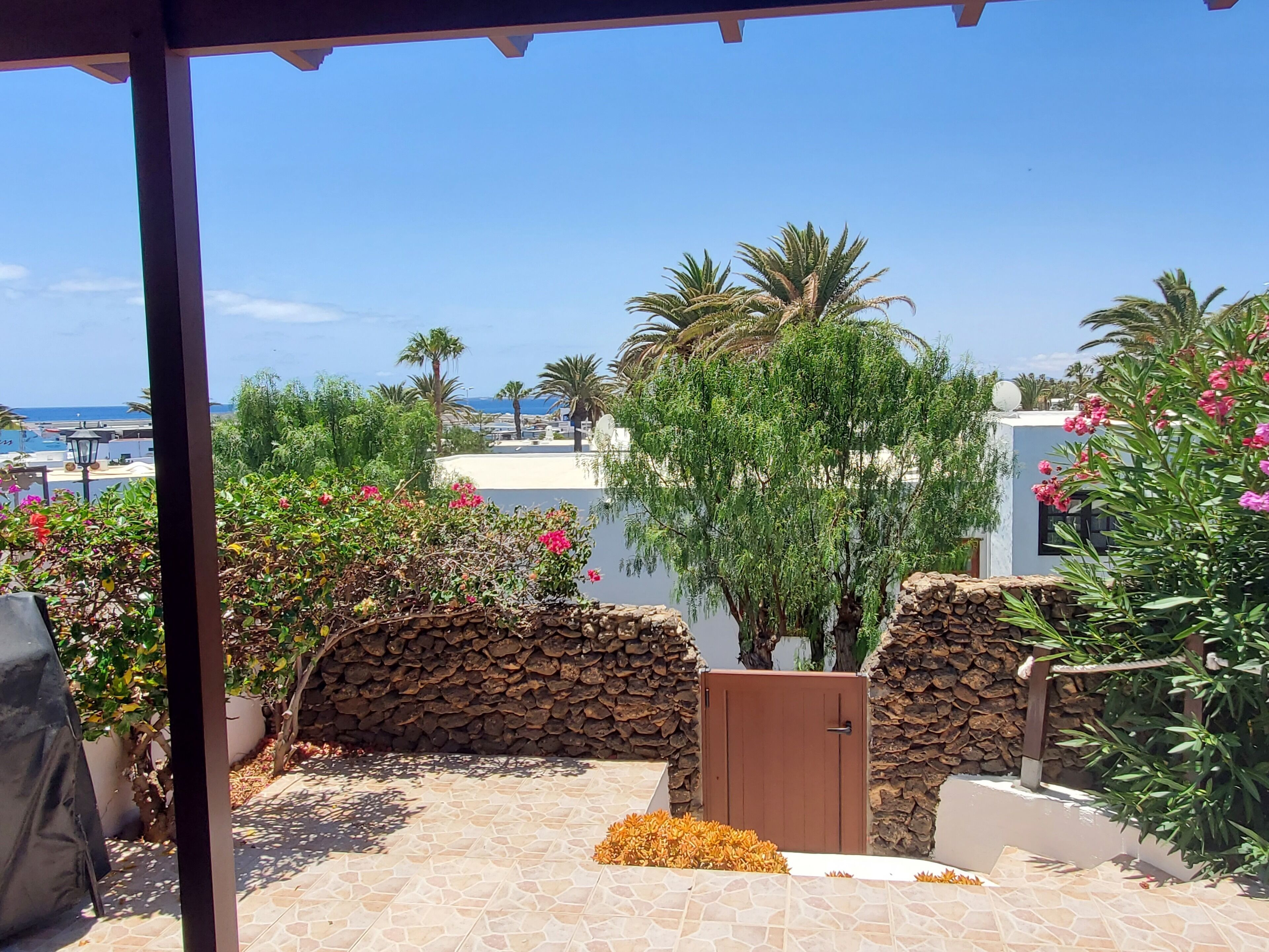A patio with stone walls, a wooden gate, and a view of the sea and beach.