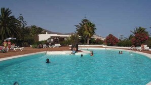 Una piscina con gente nadando y tomando el sol.
