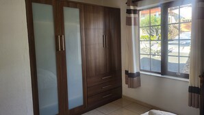 Un dormitorio con un armario grande, una cama con colcha estampada y una ventana con cortinas.
