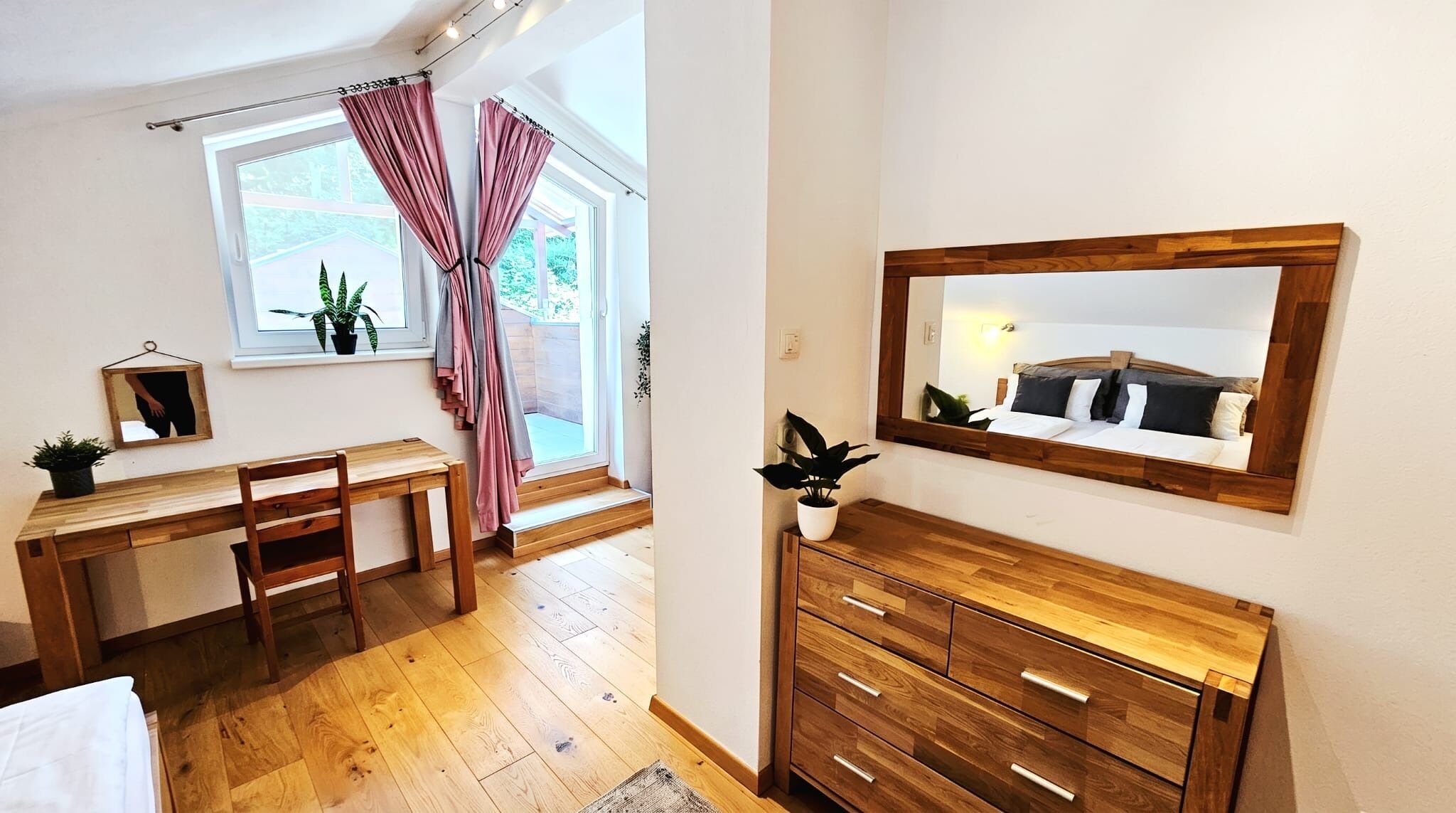 A bedroom with a wooden bed, a bedside table, a mirror, and a window with curtains.