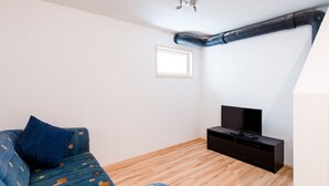 A small, well-lit room with a wooden floor, a blue sofa with patterned cushions, a black TV stand, and a small window. - Chalet Vergissmeinnicht, spacious property in Zell am See, includes Summer Card (Zell am See)
