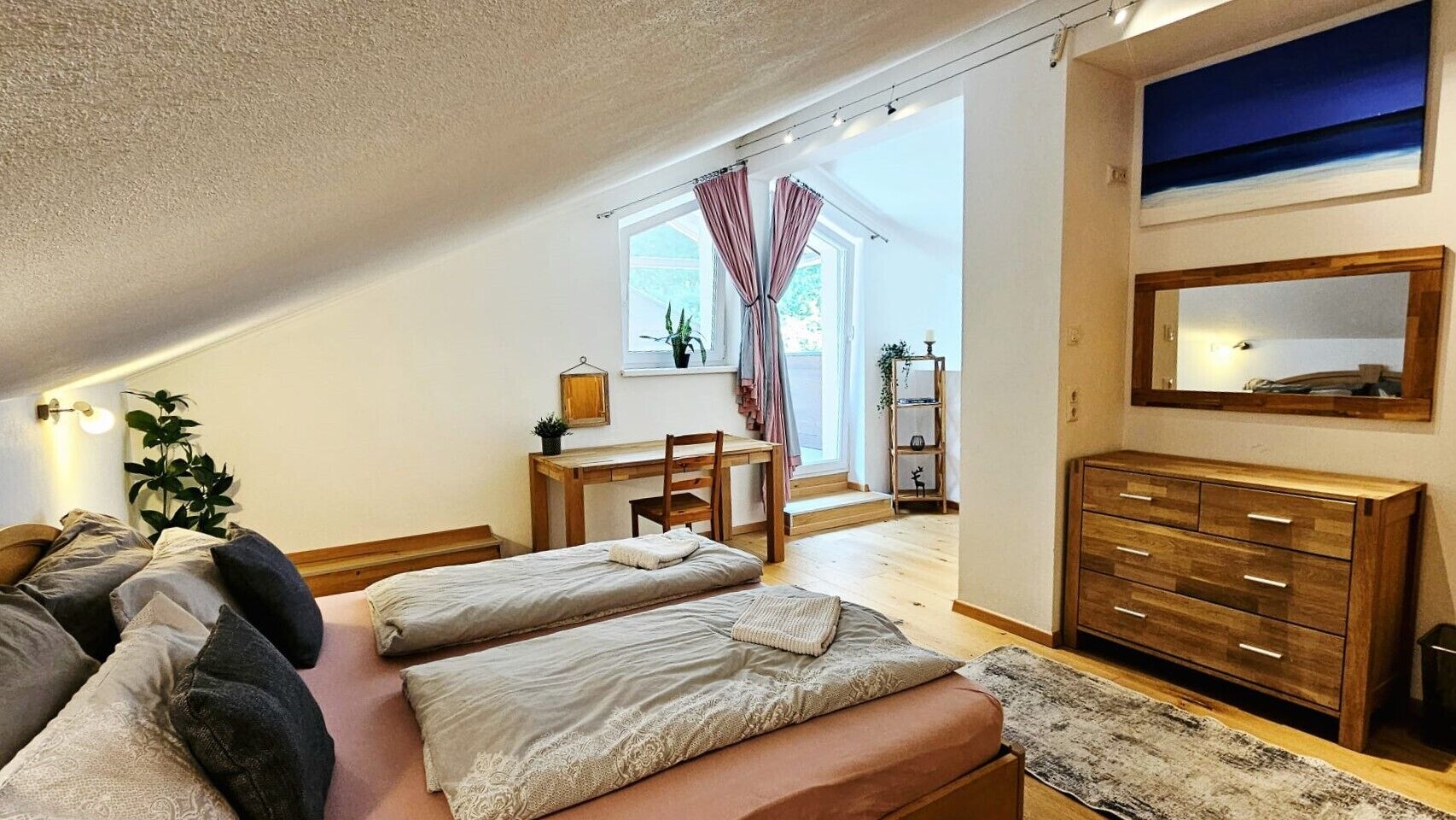 A bedroom with a bed, a desk, a chair, a dresser, and a window with curtains.