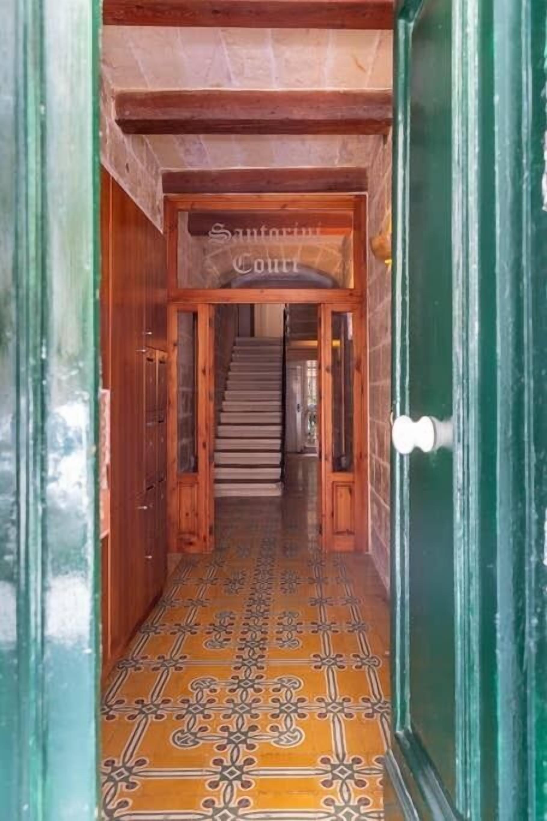 A wooden staircase leading to a room with a patterned floor and a sign that reads "Santo Antonia Court."