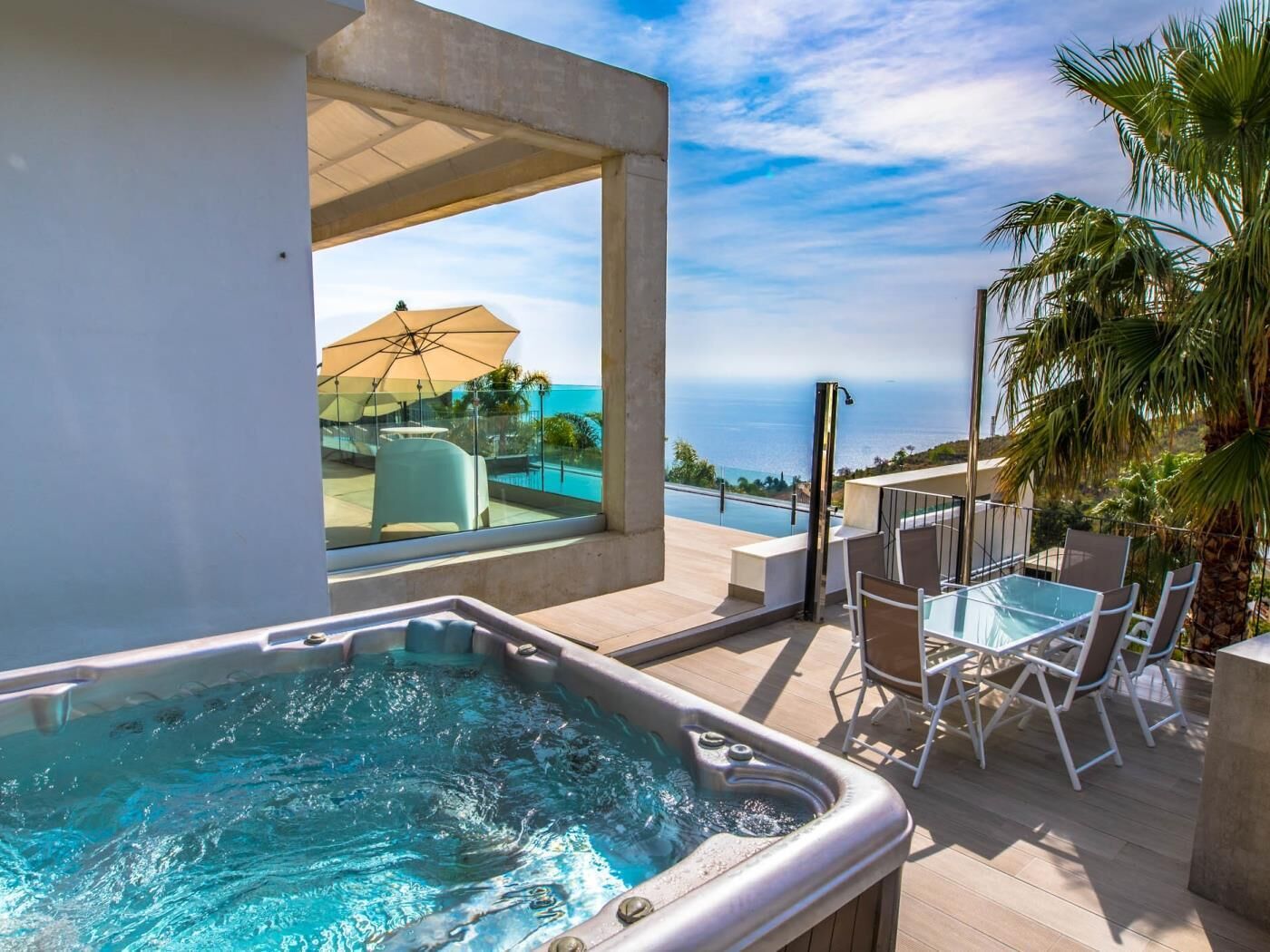 A hot tub with a view of the ocean, outdoor seating, and a covered patio area.
