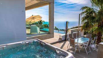 A hot tub with a view of the ocean, outdoor seating, and a covered patio area.