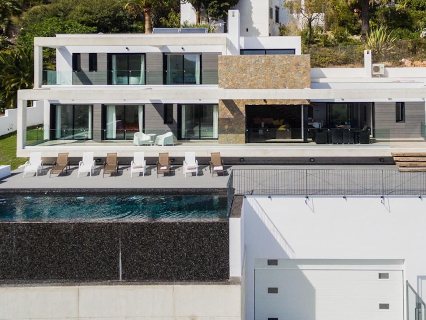 A modern two-story house with a swimming pool, large windows, and a stone facade.
