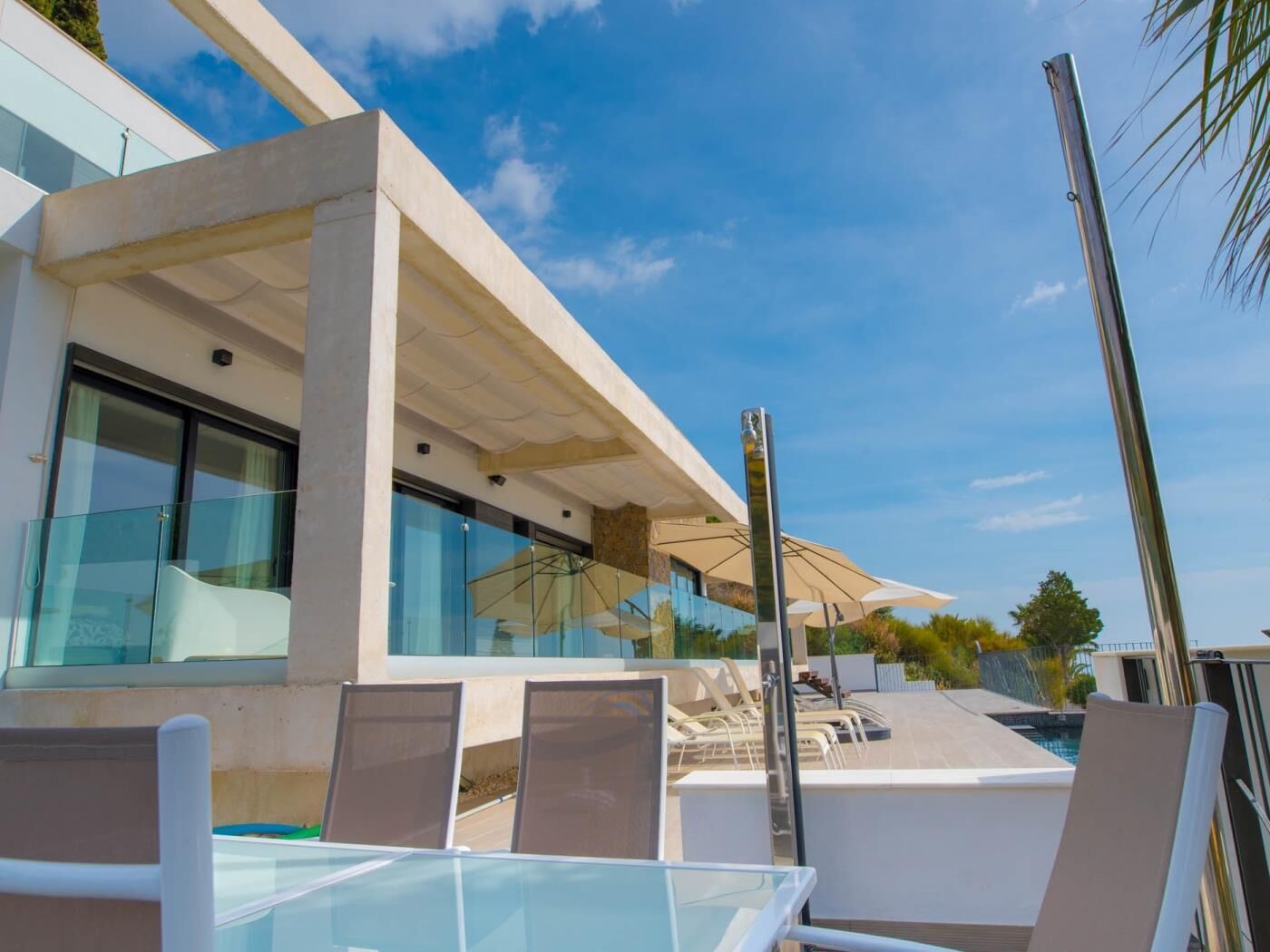 A modern outdoor seating area with glass tables and chairs, a pool, and a clear blue sky.