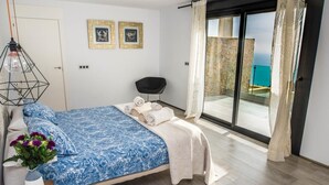 A bedroom with a bed, a chair, a vase with flowers, and a view of the sea through a sliding door. - Luxury villa with heated pool and sea views (Salobreña)