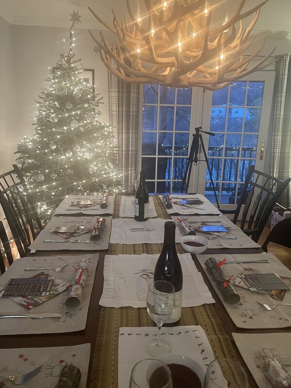 Un coin repas agrémenté d’un sapin de Noël, d’un lustre et offrant une vue sur l’extérieur par une fenêtre.