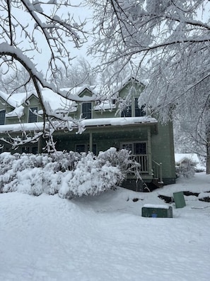 Une maison recouverte de neige, avec un petit porche et une porte verte.