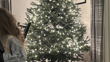 A Christmas tree with lights and ornaments, a framed picture on the wall, and a glass jar with decorations on the floor.