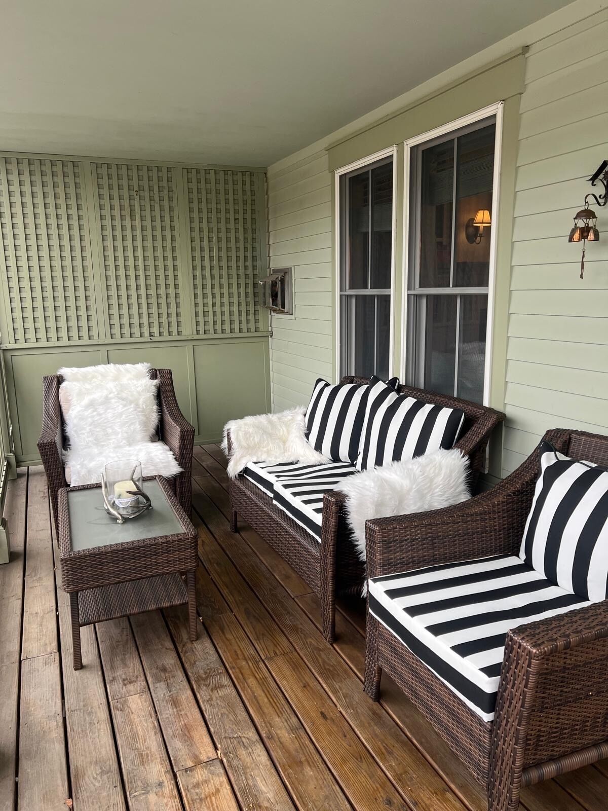 A cozy porch with wicker furniture, a glass table, and a window with a lamp.
