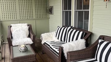 A cozy porch with wicker furniture, a glass table, and a window with a lamp.