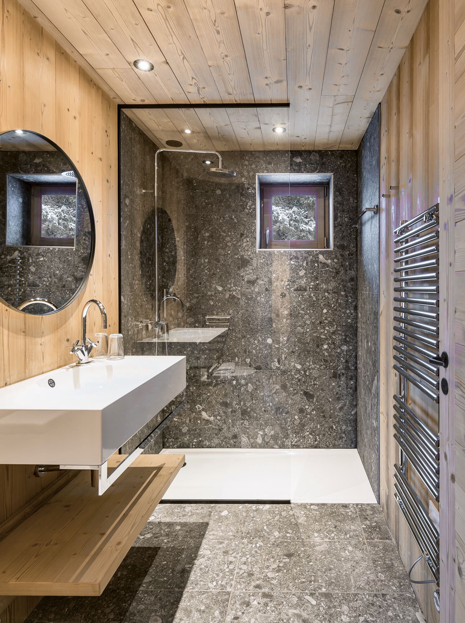 A modern bathroom with a wooden ceiling, a large mirror, a white sink, a shower, and a built-in heater.