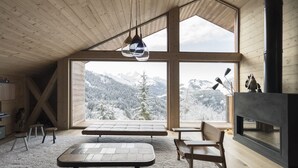 A cozy cabin interior with a large window offering a snowy mountain view, a fireplace, and a wooden ceiling. - Barma Chalet - Luxurious modern chalet, exceptional view, 900 m from the slopes (Manigod)