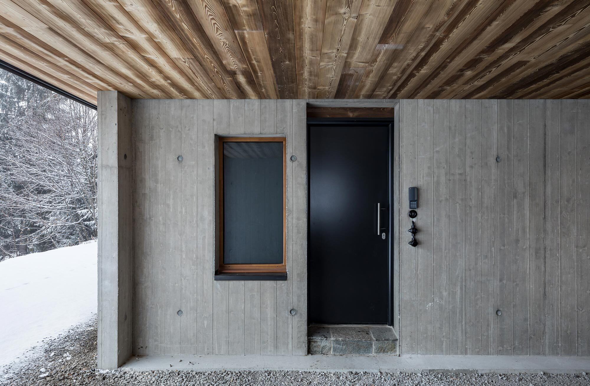 A modern exterior with a concrete facade, a wooden ceiling, a door with a handle, and a small step leading to the entrance.