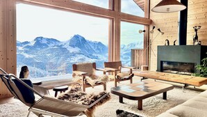 A cozy living room with a large window offering a mountain view, wooden furniture, and a fireplace. - Barma Chalet - Luxurious modern chalet, exceptional view, 900 m from the slopes (Manigod)