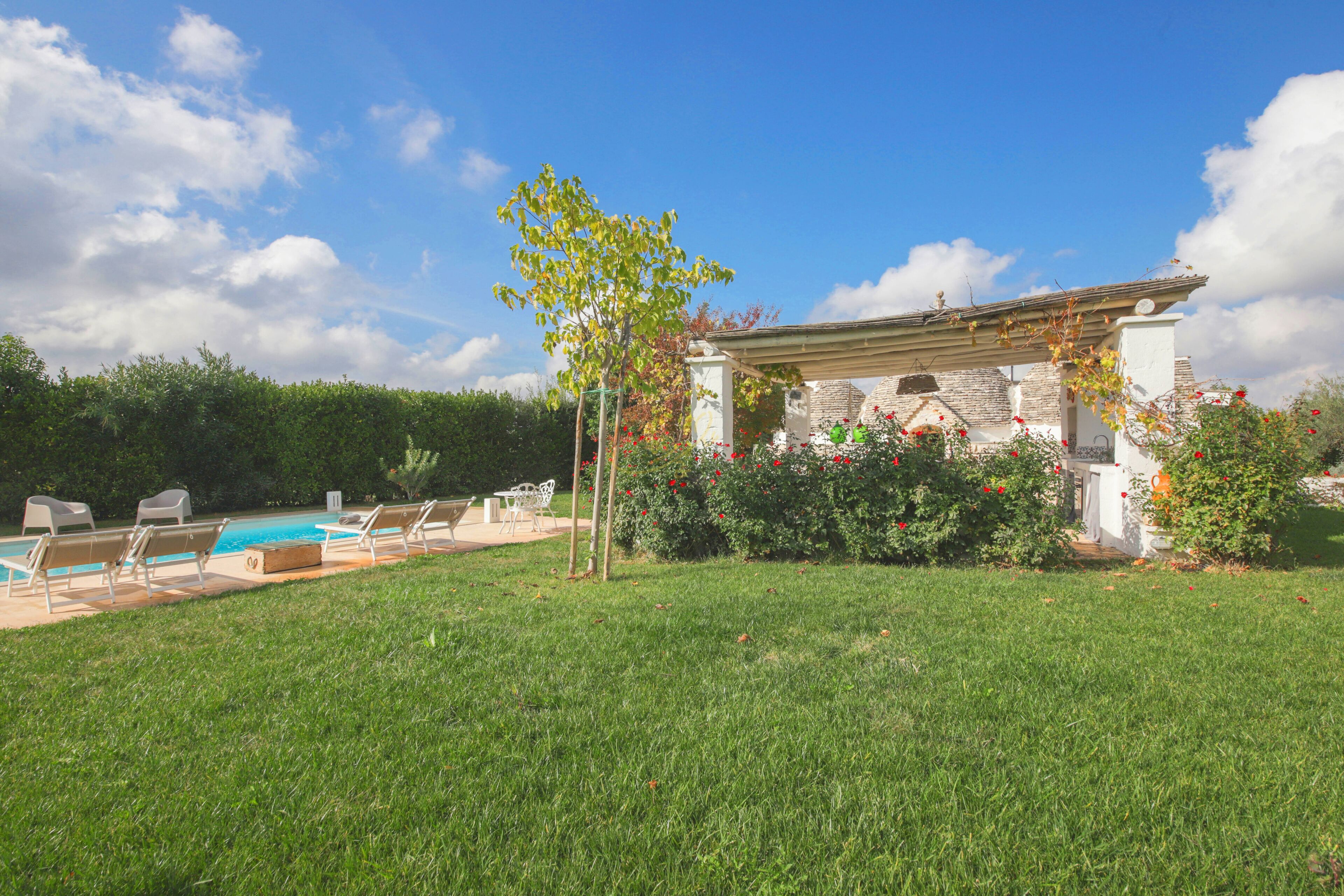Ein Poolbereich mit Liegestühlen, einer Pergola und einem Steinhaus mit Garten.