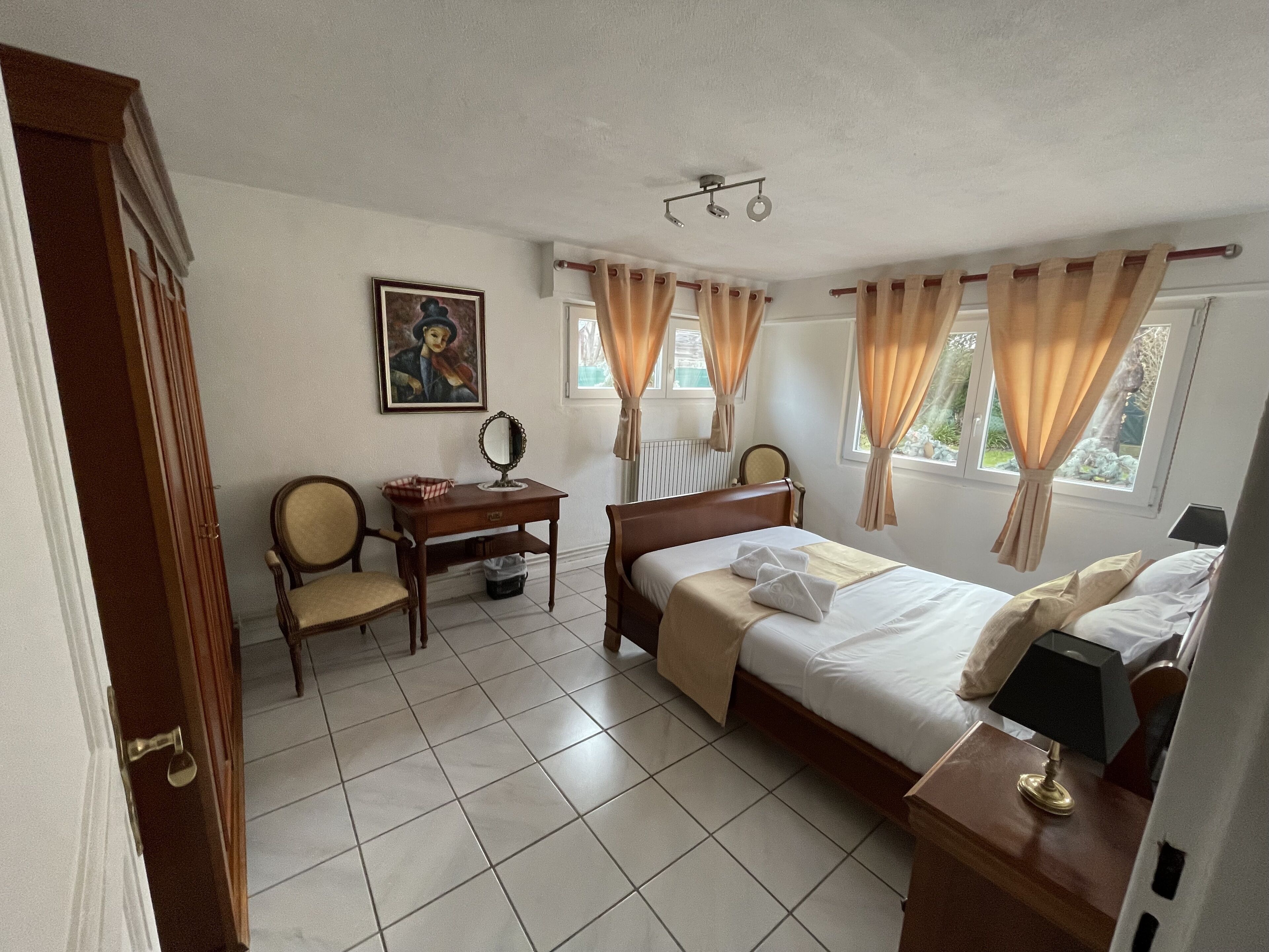 A hotel room with a bed, a desk with a mirror, a chair, and a painting on the wall.