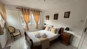 A bedroom with a wooden bed, a chair, a nightstand, and a window with curtains.