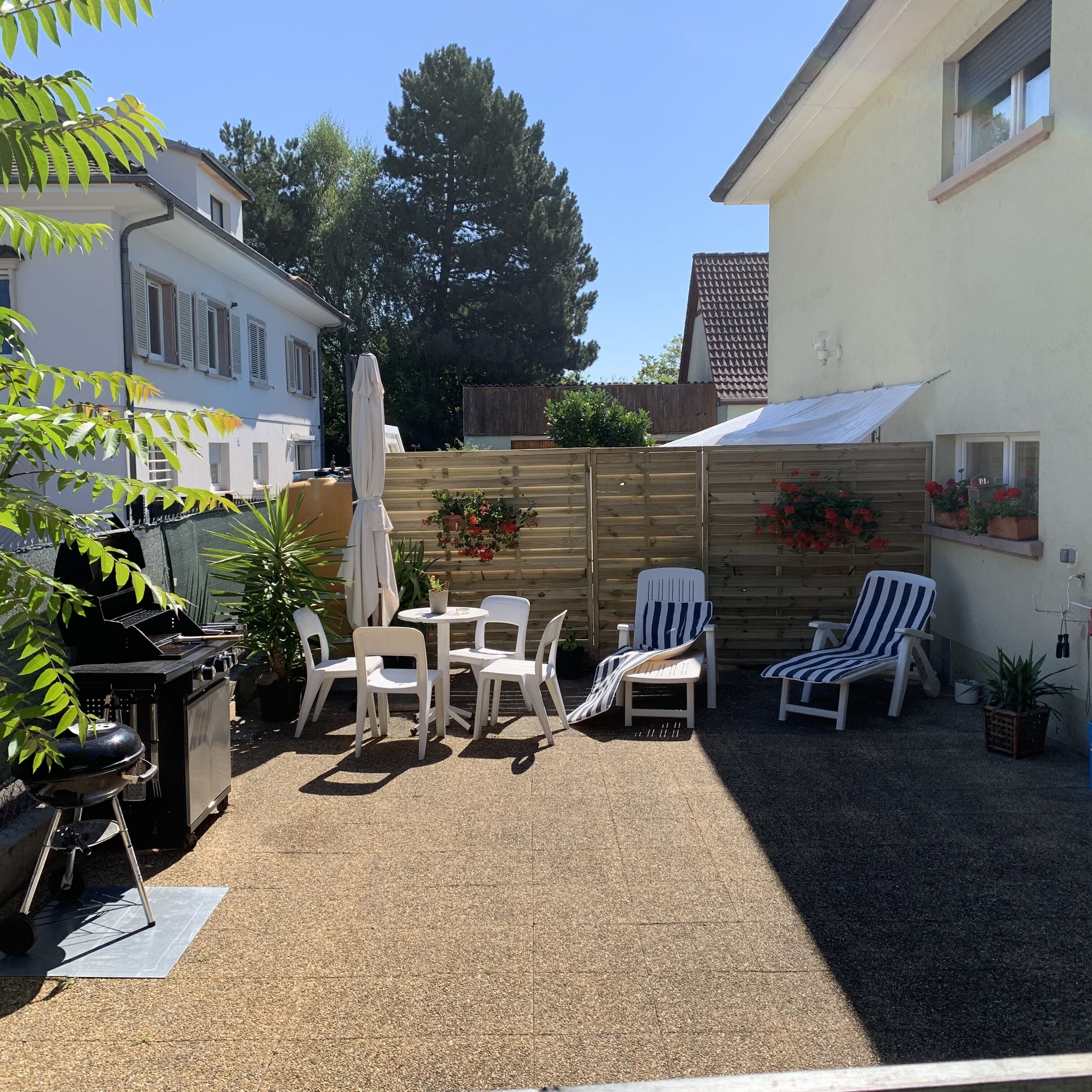 Eine Terrasse mit Grill, weißen Plastikstühlen und einem Tisch.