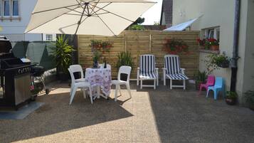 En terrasse med et bord, stole, grill og plantekasser.