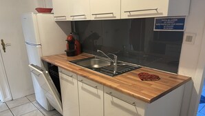 A compact kitchen with white cabinets, a stainless steel sink, and a wooden countertop.